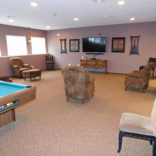 A spacious game room featuring a pool table, several armchairs, and a large television.