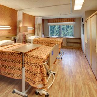 A hospital room with two neatly made beds and a large window providing natural light.