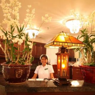 A hotel receptionist standing behind the front desk adorned with plants and a decorative lamp.