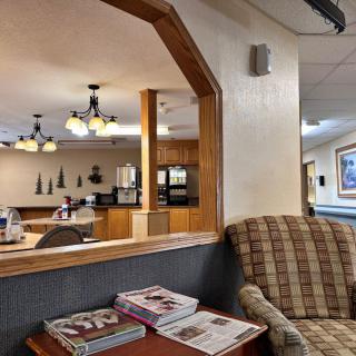 A cozy waiting area with a comfortable chair, a table with magazines, and a view into a well-lit dining or meeting room.