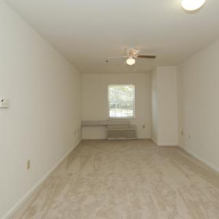 An empty room with a window, ceiling fan, and carpeted floor.