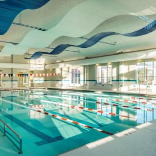 A spacious indoor swimming pool with lane dividers and a wave-themed ceiling design, illuminated by abundant natural light.