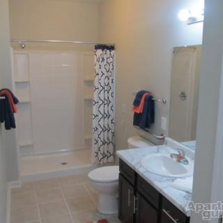 A clean, modern bathroom featuring a shower with a patterned curtain, a sink with a marble countertop, and a toilet.