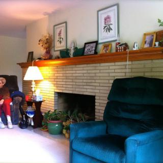 A cozy living room with a fireplace, armchair, and various decorations on the mantel.