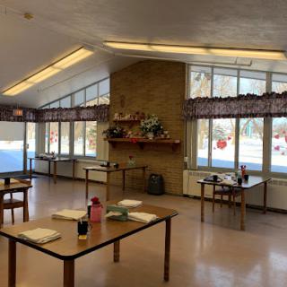 A spacious, well-lit room featuring several tables and large windows, adorned with decorative elements.