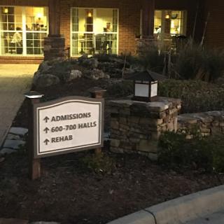 A directional sign indicating the way to admissions, dining, and other services at night.