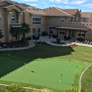 A luxury home with a backyard featuring a golf putting green and patio area.
