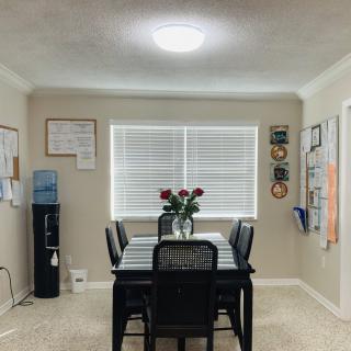 A cozy dining room with a table set for six, featuring a vase of roses and adorned with wall decorations.