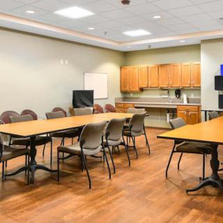 A spacious conference room with tables and chairs arranged for a meeting, featuring a TV screen and whiteboard.