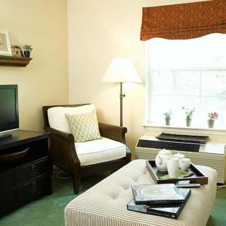 A cozy living room with modern furniture, featuring a television, armchair, and natural light from the window.