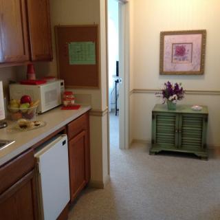 A cozy kitchen area with wooden cabinets, a microwave, and decorative elements like flowers and artwork.