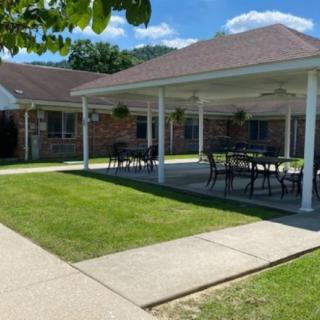 A covered patio area with tables and chairs next to a building, surrounded by a green lawn.