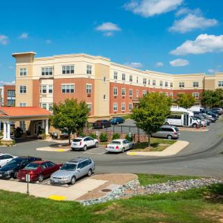A large, multi-story building with a parking lot and several cars under a clear blue sky.