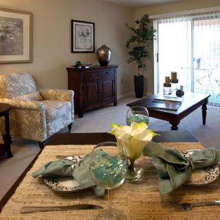 A cozy living room with a dining table set for two, featuring elegant decor and natural lighting.