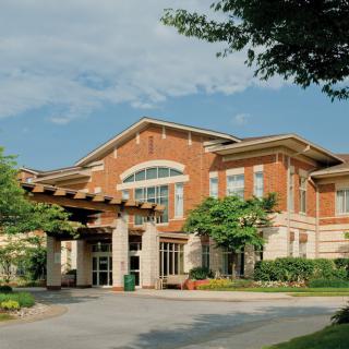 A two-story brick building with a prominent entrance, surrounded by trees and set against a clear blue sky.