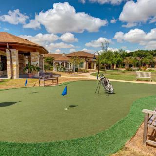 A sunny day on the putting green with a clubhouse in the background.