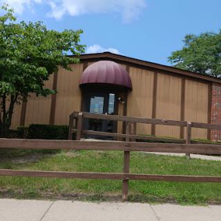 A peaceful view of a building with a brown awning, surrounded by greenery and a wooden fence.