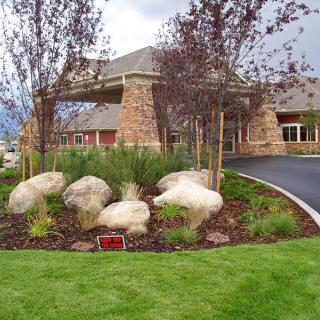A beautifully landscaped building entrance with boulders, greenery, and stone architecture.