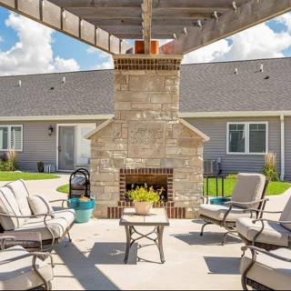A cozy outdoor patio with a central fireplace and comfortable seating under a pergola.