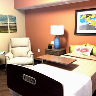 A well-decorated hospital room featuring a patient bed, a comfortable chair, and colorful artwork.