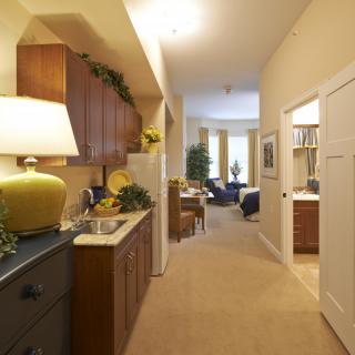 A cozy apartment interior featuring a compact kitchen and a hallway leading to the living room.
