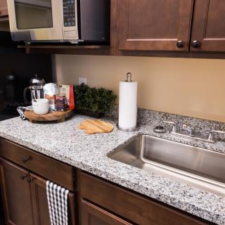 A modern kitchen countertop with a sink, microwave, and various items including a coffee maker and cutting board.