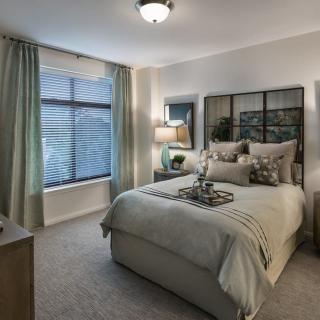 A cozy and modern bedroom featuring a neatly made bed with decorative pillows, a bedside lamp, and large window drapes.