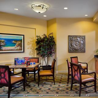 A cozy lobby seating area with chairs, tables, wall art, and a potted plant.