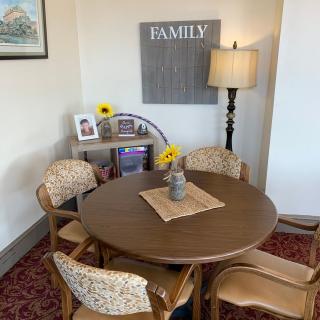 A cozy living room corner with a round table surrounded by chairs, accented with a lamp and a 'Family' sign on the wall.