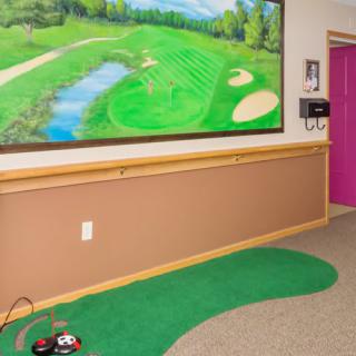An indoor hallway features a putting green and a vibrant golf course mural on the wall.