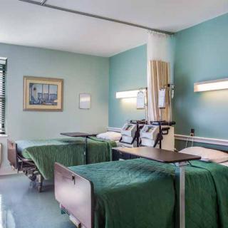 An empty hospital room with two patient beds and green walls.