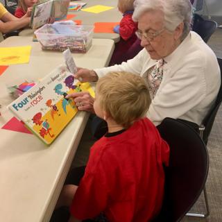 An adult reading a book to a child at a table.