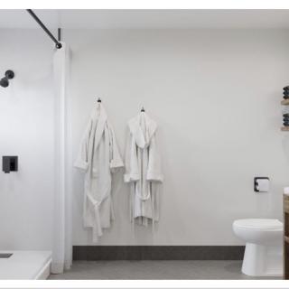 A modern and minimalist bathroom with white walls and two robes hanging on the wall.