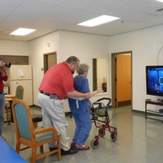 A caregiver assists an elderly person with walking using a walker in a care facility.