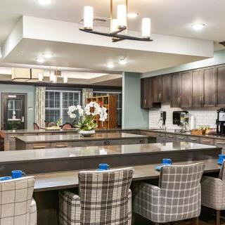A modern kitchen with a large central island, surrounded by plaid upholstered chairs and featuring sleek dark cabinetry.