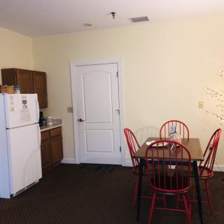 A small kitchen area with a white refrigerator, wooden cabinets, and a dining table with red chairs.