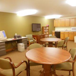 A spacious office break room with tables, chairs, a computer setup, and a kitchenette.