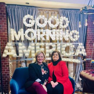 Two women posing together in front of a 'Good Morning America' backdrop.