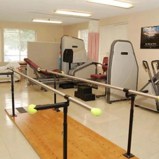 A physical therapy room equipped with exercise machines and parallel bars for rehabilitation.