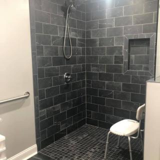 A modern walk-in shower with black tiles and a built-in seat.