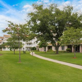 A scenic view of a grassy area with a walkway, surrounded by trees and residential buildings.