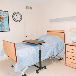 A clean and organized hospital room featuring a patient bed with a blue blanket, a bedside table, and a wall clock.