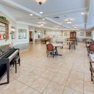 A spacious room with a piano, tables, and chairs arranged on tiled flooring.