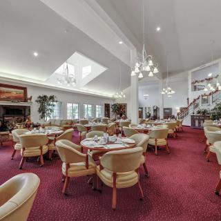 A spacious restaurant dining area with elegant chandeliers, comfortable seating, and a red carpeted floor.