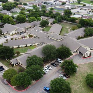 Aerial view of a suburban residential complex with surrounding trees and a parking area.