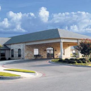 A large building with a covered entrance and surrounding landscape under a partly cloudy sky.
