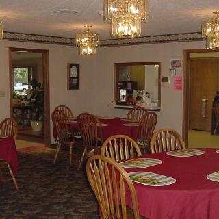 A cozy dining area with wooden tables and chairs, adorned with red tablecloths and lit by chandeliers.