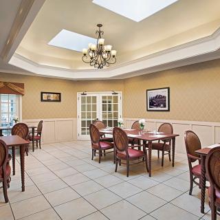 An elegant dining room with multiple tables and chairs, featuring a chandelier and skylights.