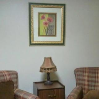 A cozy interior setup with two plaid chairs, a side table with a lamp, and a framed painting on the wall.