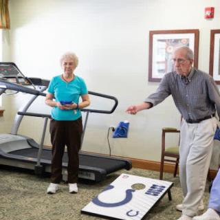 Two seniors enjoying a game of cornhole in an exercise room.